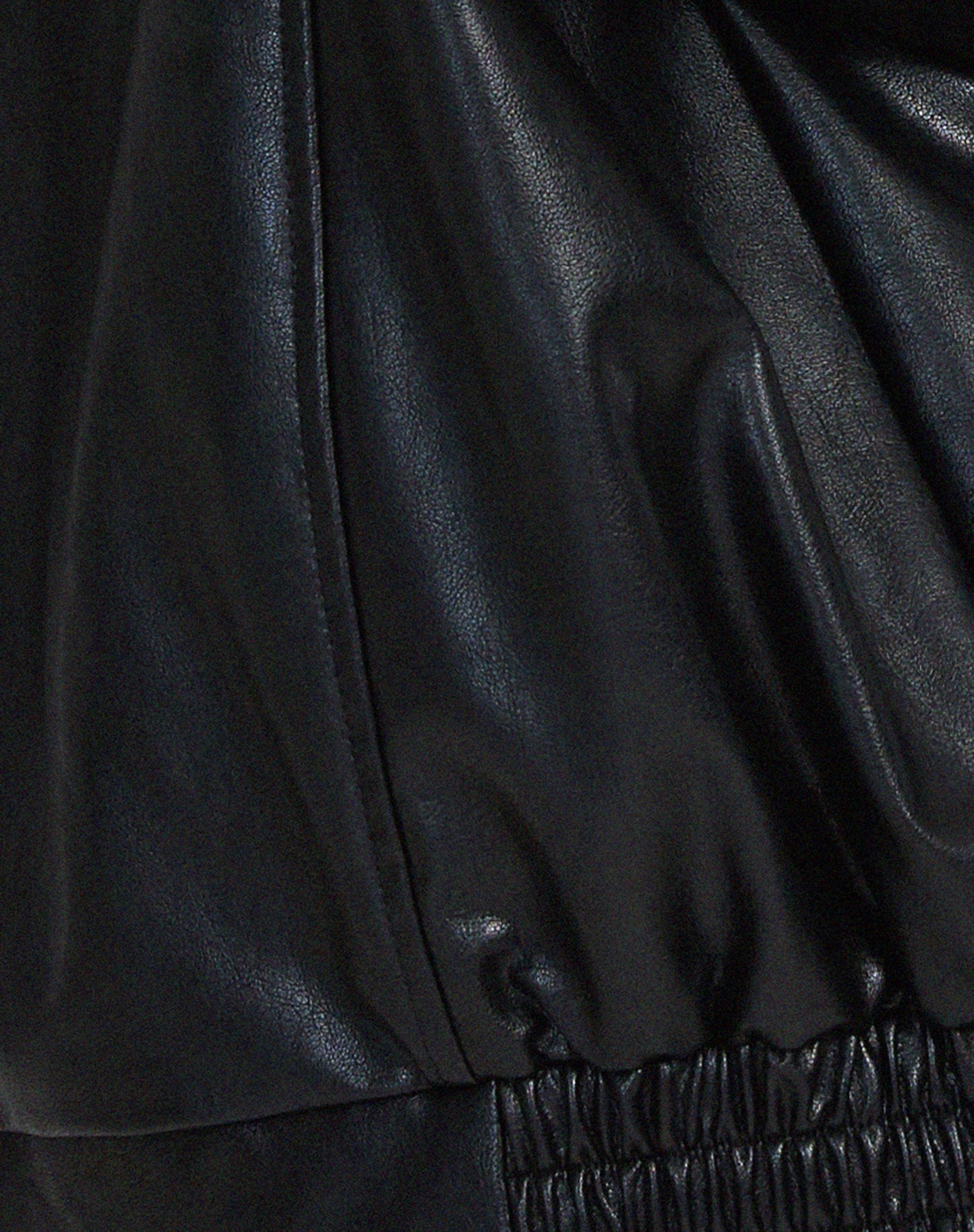 Black PU leather jacket fabric close-up with seam stitching and elastic hem band.