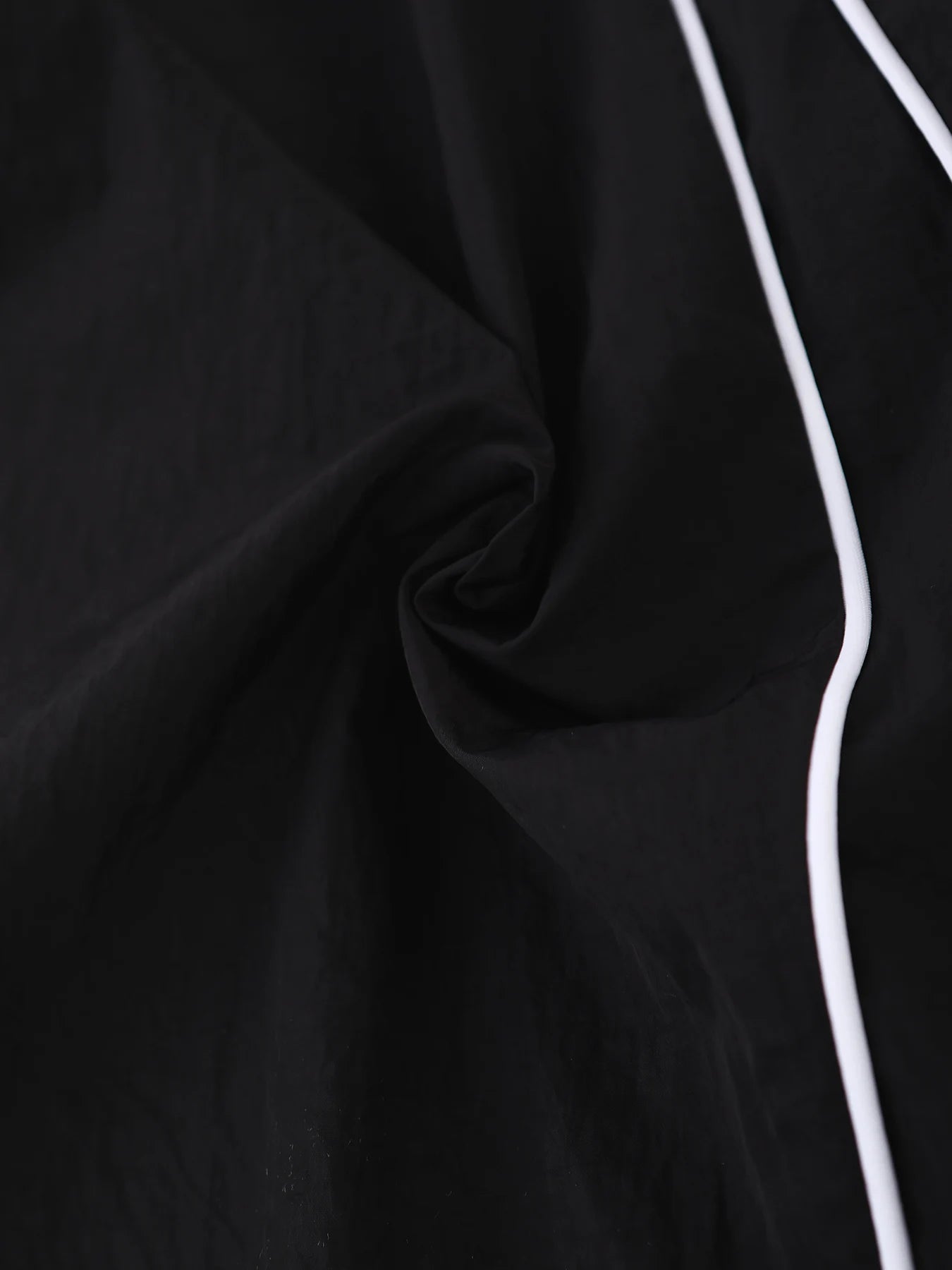 Black wide-leg trousers fabric close-up with stitched side seam and white piping