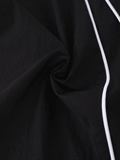 Black wide-leg trousers fabric close-up with stitched side seam and white piping