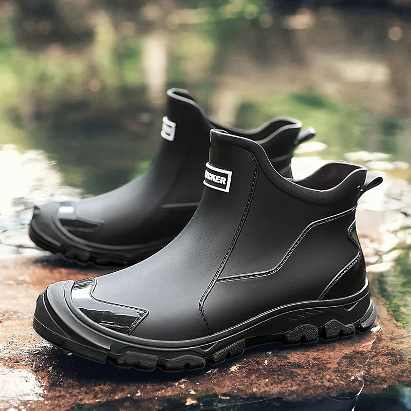 Men's waterproof black ankle boots with pull tabs and red rugged outsole on wet ground