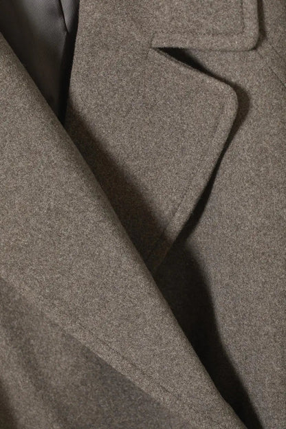 Grey wool coat fabric close-up with textured weave and diagonal seam detail.