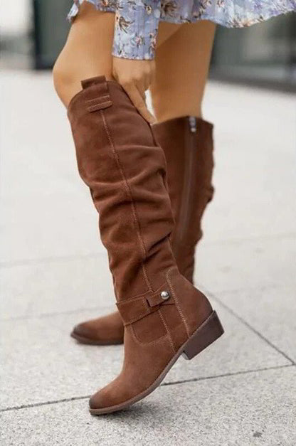 Brown knee-high flat boots with side buckle strap and stitched panels