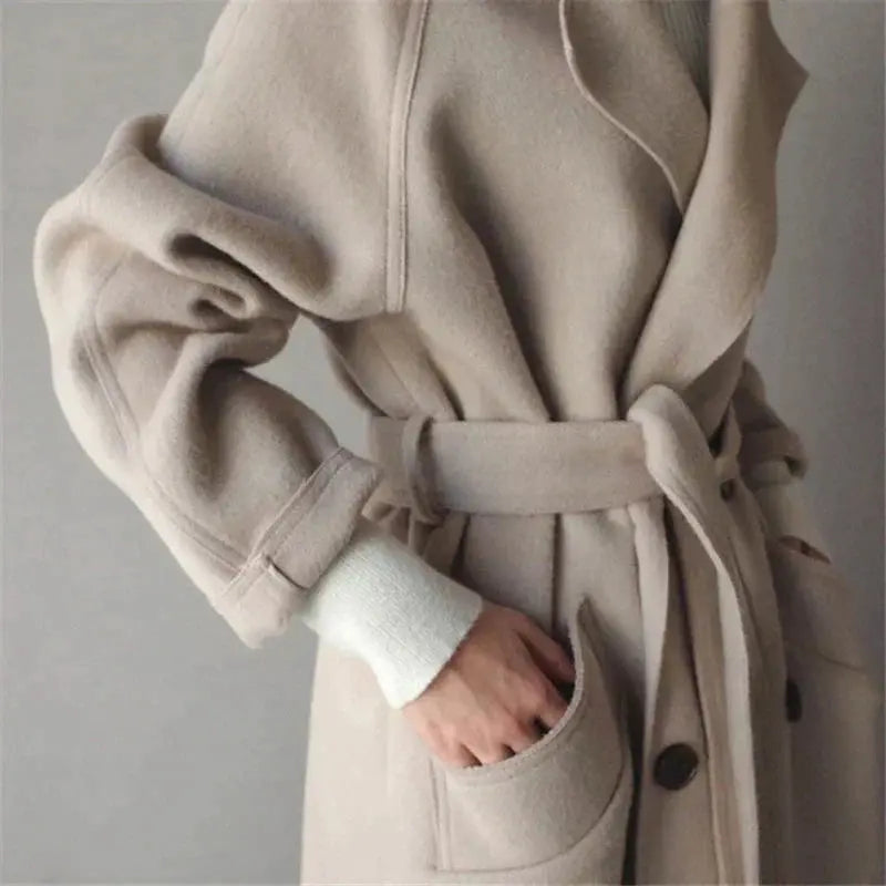 Beige long wool coat detail: wrap-style collar, belt tie, and buttoned pocket opening