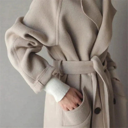 Beige long wool coat detail: wrap-style collar, belt tie, and buttoned pocket opening