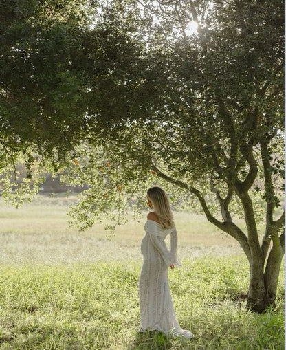 White lace off-shoulder maternity dress with long sleeves and flowing skirt, back/side view
