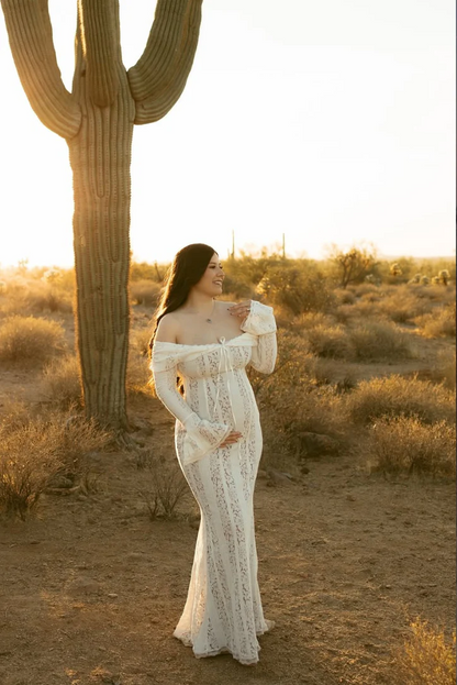 White lace maternity dress with off-shoulder neckline and long sleeves, full-body standing pose