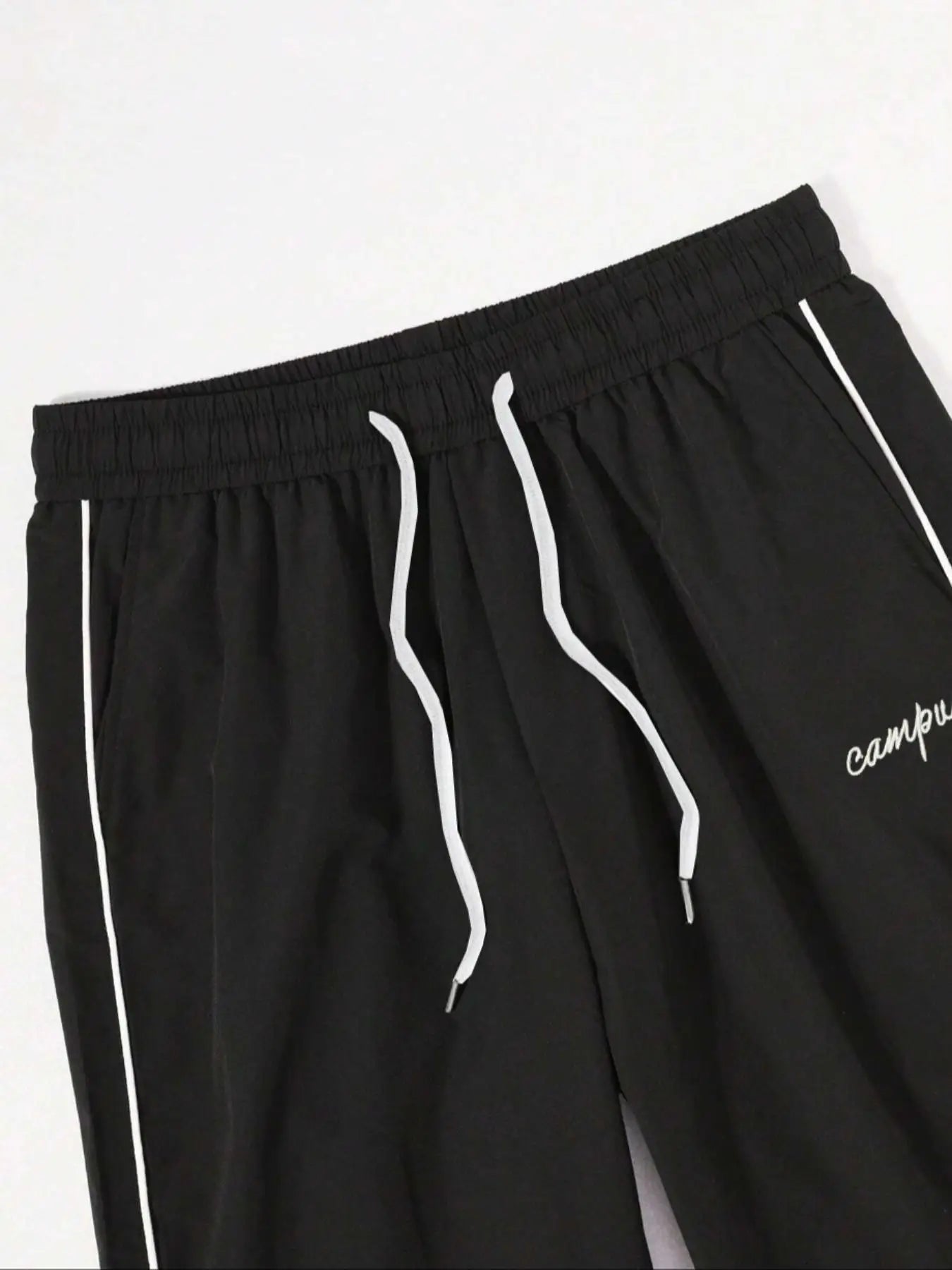 Black quick-dry trousers close-up: elastic waist, drawstring ties, white side stripes.