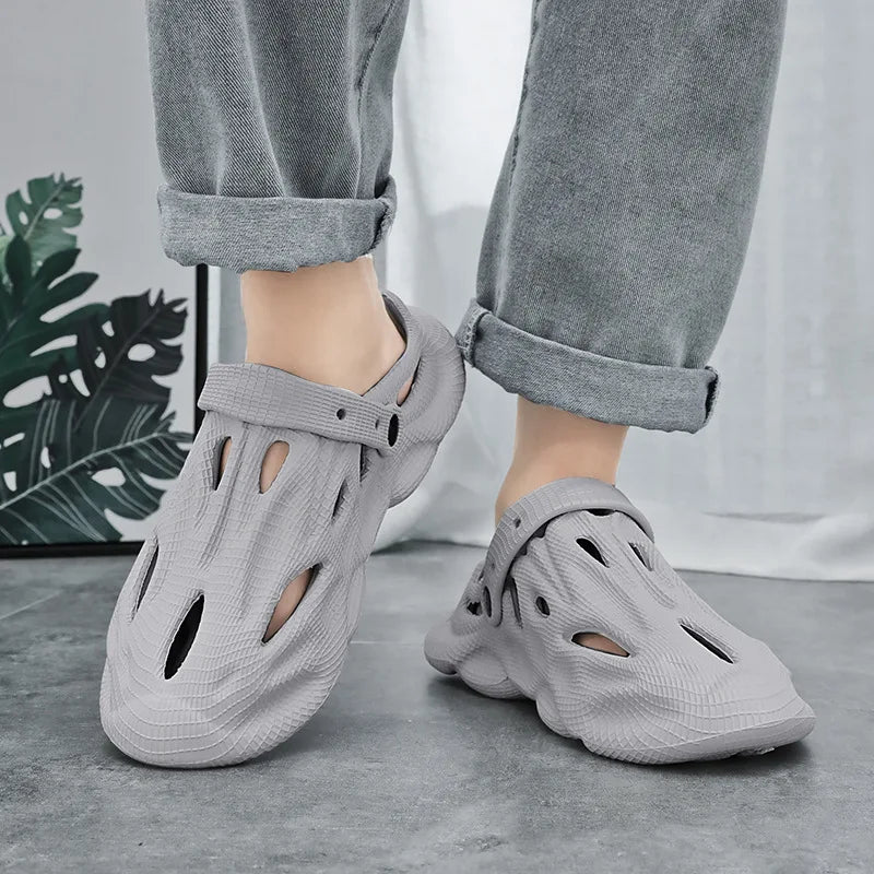 Light gray hollow garden clogs with oval cutouts and strap, worn with pants
