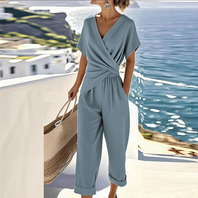 Dusty blue wrap jumpsuit with V-neck, short sleeves, draped waist, wide cropped legs