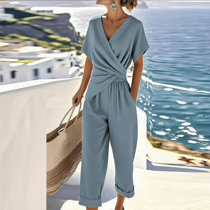 Dusty blue wrap jumpsuit with V-neck, short sleeves, draped waist, wide cropped legs