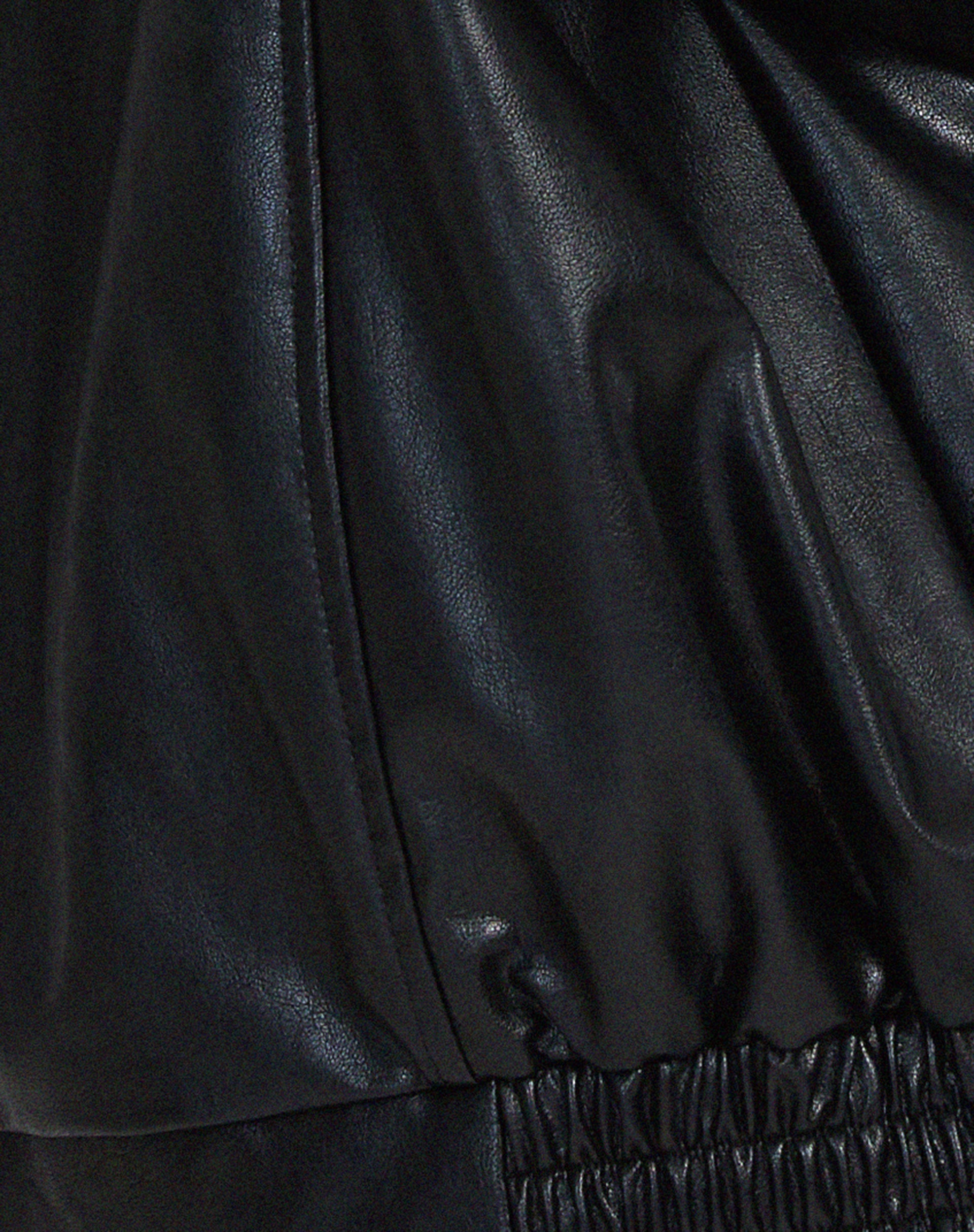 Black PU leather jacket fabric close-up with seam stitching and elastic hem band.