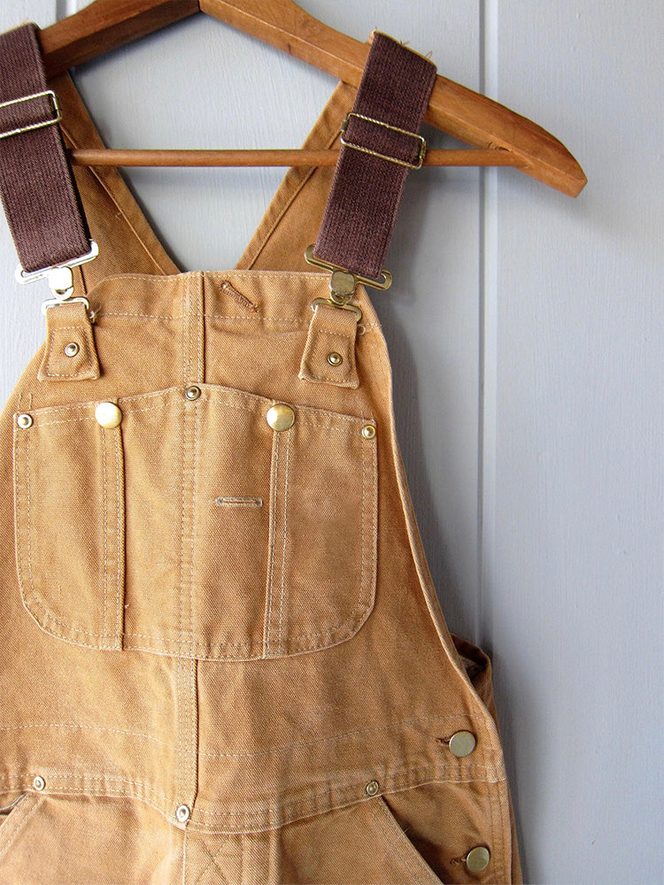 Men's camel canvas bib overalls close-up with adjustable straps and front pocket