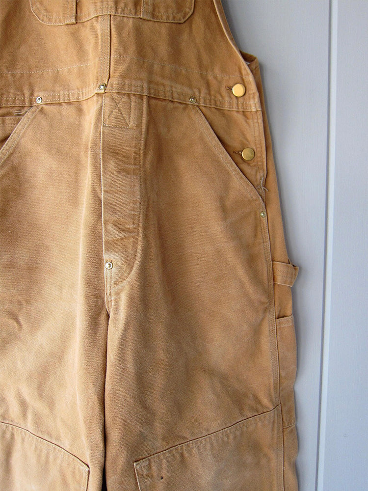 Men's camel canvas overalls close-up with front seam, buttons, and side pocket