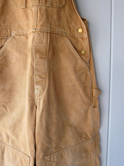 Men's camel canvas overalls close-up with front seam, buttons, and side pocket