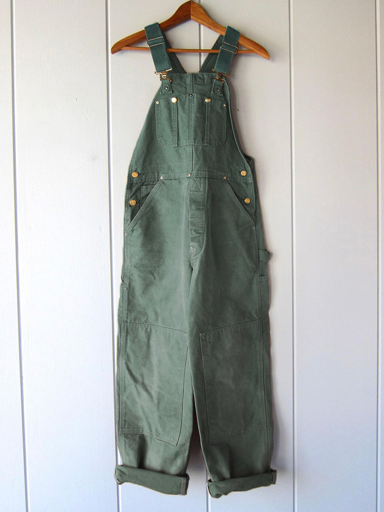 Men's dark green canvas bib overalls with adjustable straps and front utility pockets
