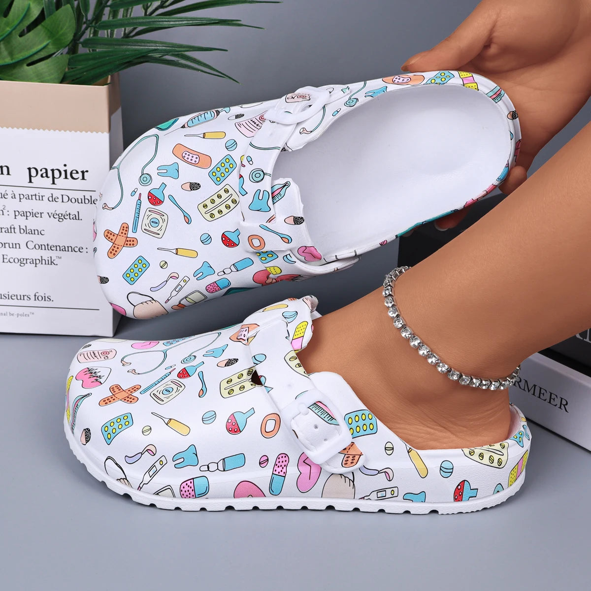 White medical-print nurse clogs, open mule with adjustable buckle strap.