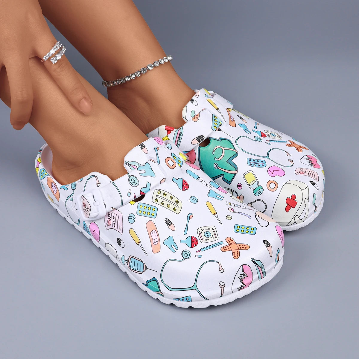 White medical-print nurse clogs with adjustable buckle and textured anti-slip sole.