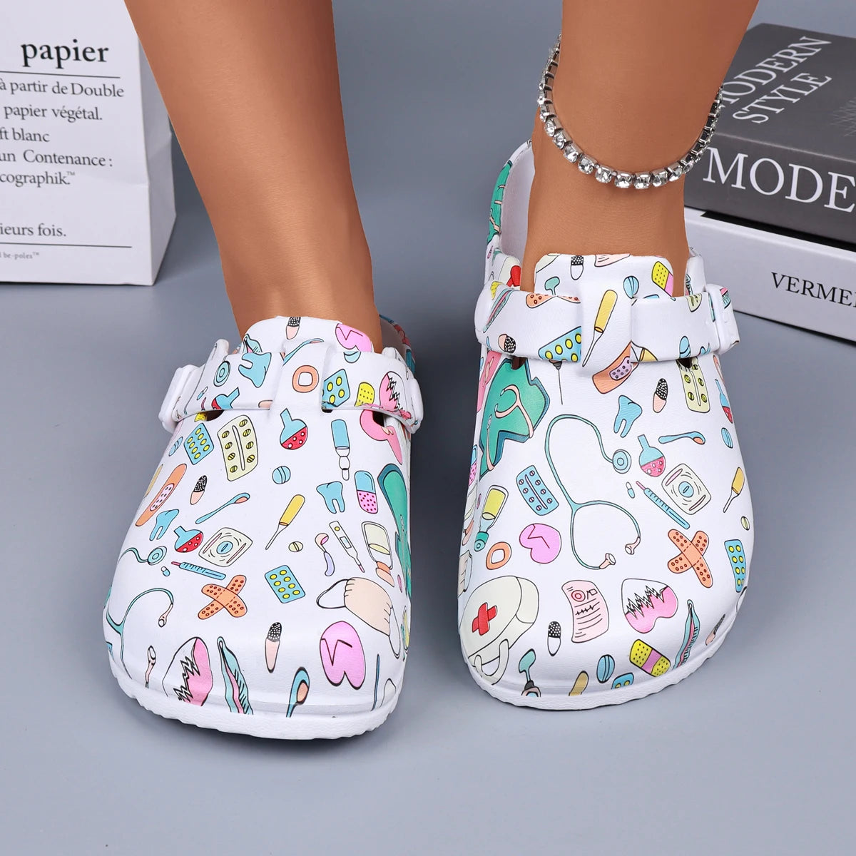 White medical-print nurse clogs with adjustable buckle straps, front view on feet.