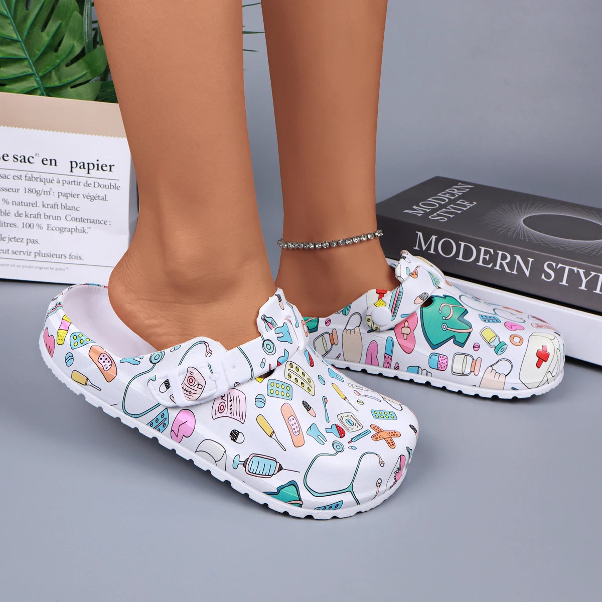 White medical-print nurse clogs on feet, adjustable buckle strap and grippy sole.