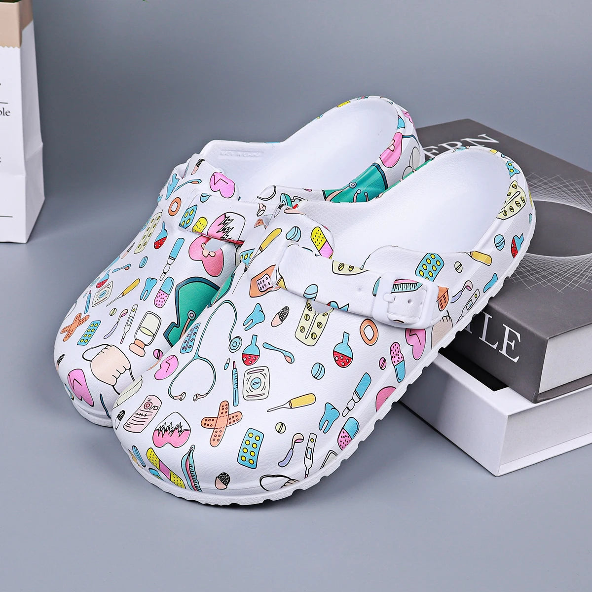 White medical-print nurse clog pair, open mule with adjustable buckle detail.